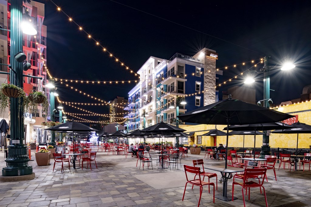a plaza at night with red chairs and umbrellas and street lights