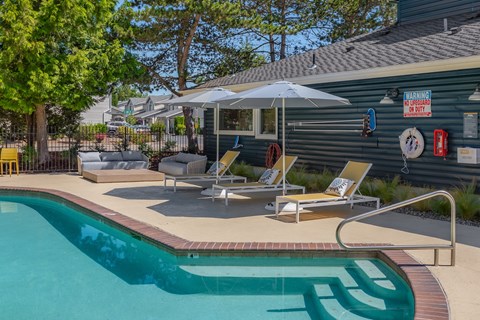 A pool with a sun lounger and umbrella next to a building.
