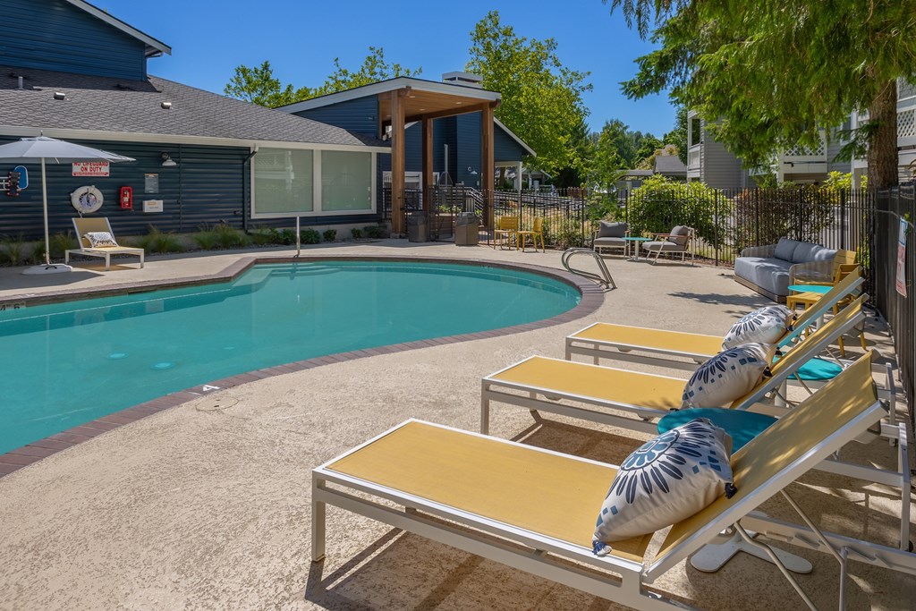 A pool with sun loungers and a building in the background.