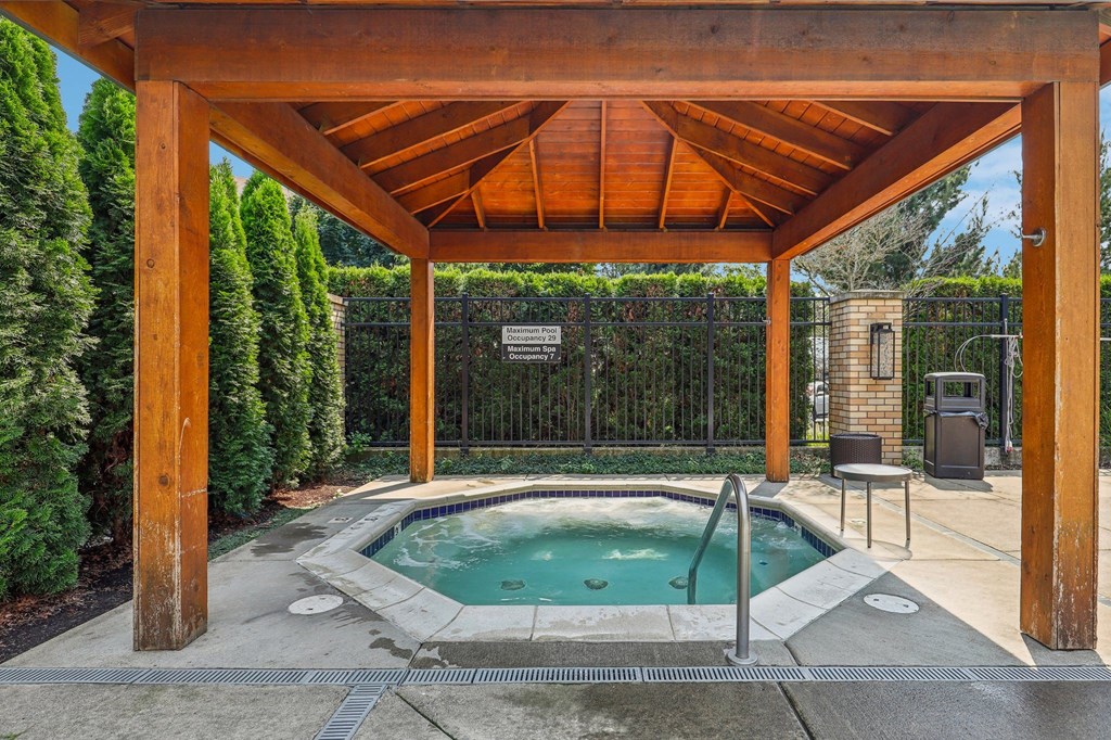 a hot tub is under a wooden pavilion next to a pool