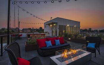 a rooftop patio with a fire pit and chairs at dusk