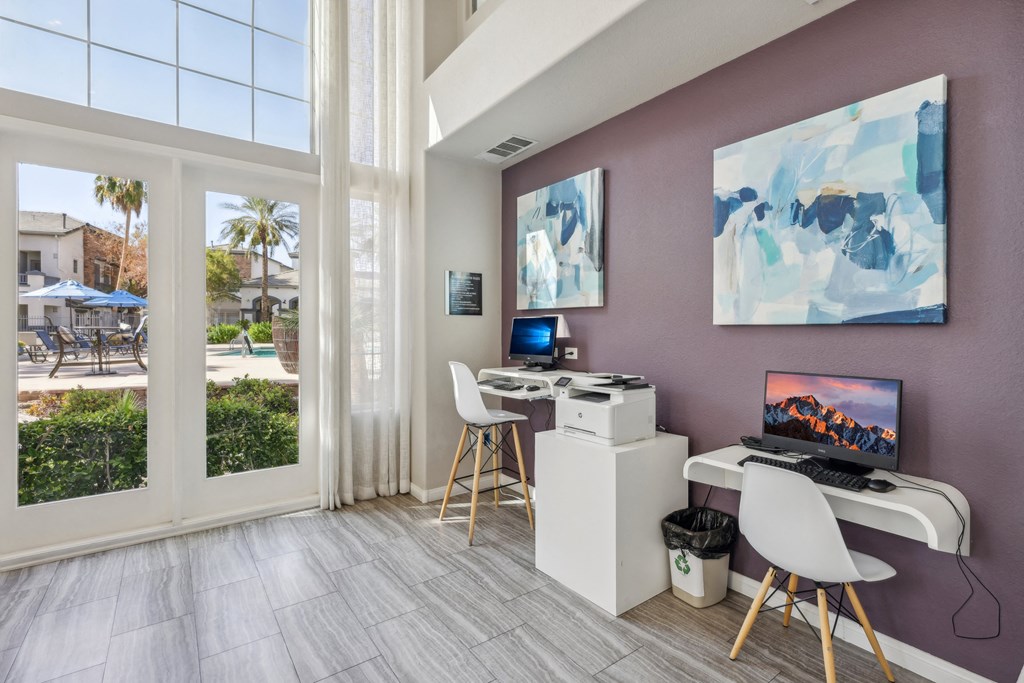 a room with a desk with a computer and chairs and a window