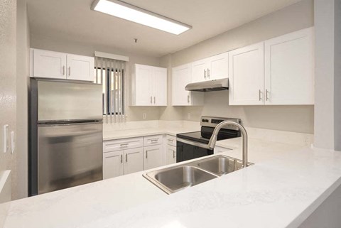 a white kitchen with a sink and a stainless steel refrigerator