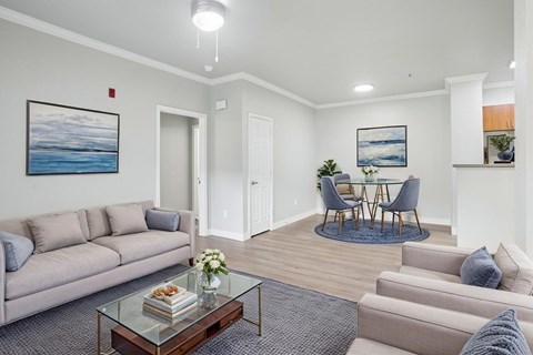 A living room with a grey sofa, a glass coffee table, and a painting of a beach scene on the wall.