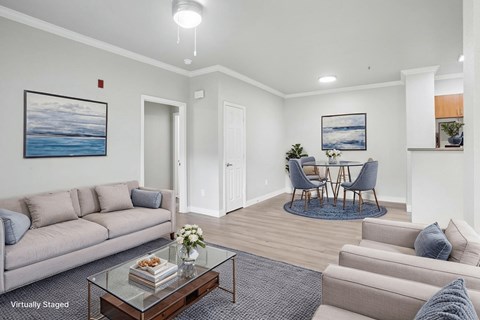 A living room with a grey couch, a glass coffee table, and a painting of a beach scene on the wall.