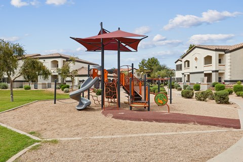 A playground with a red umbrella and a slide.