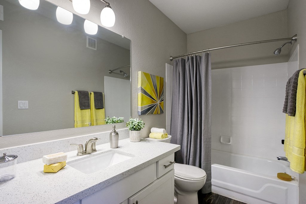 Master bathroom with floating vanities, quartz countertops, backlit vanity mirror, walk-in shower with Euro shower door and quartz-topped bench seat at Sonoran Apartment Homes, Phoenix, AZ