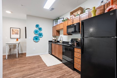 A black refrigerator is in the corner of a kitchen with wooden floors and white walls.
