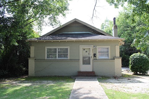a small tan house with a sidewalk in front of it