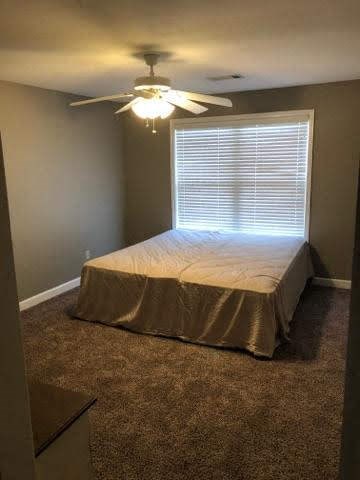 A bedroom with a bed covered in a tan sheet and a ceiling fan with lights.