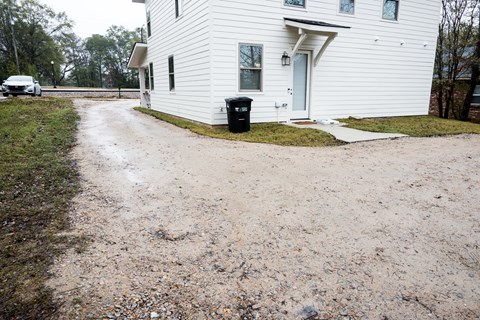 A white house with a black trash can in front of it.