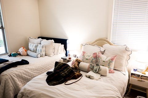 A bedroom with two beds and a window with blinds.