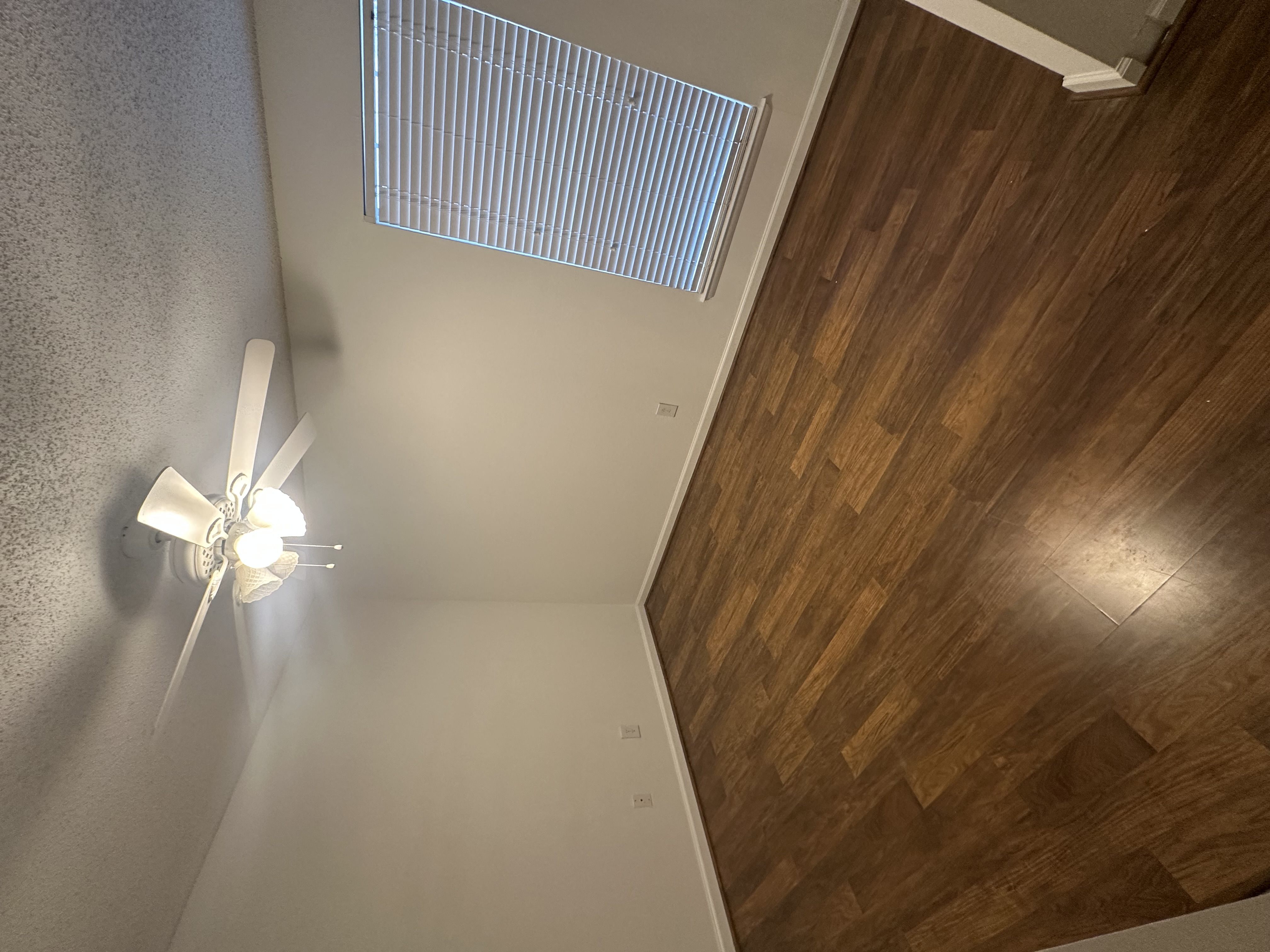 A ceiling fan with lights is mounted on a wall above a wooden floor.