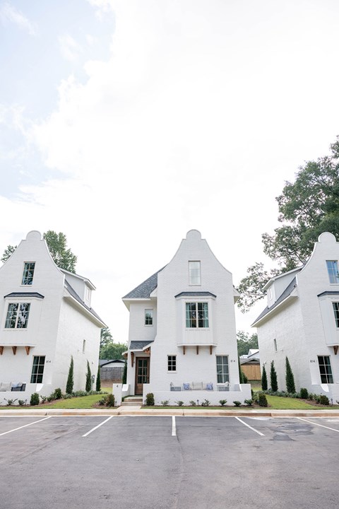 Three white houses with black trim and windows are in front of a tree.