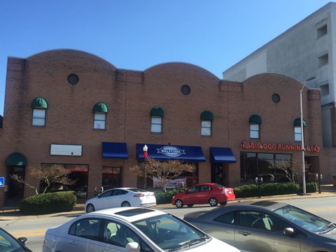 A red car is parked in front of a building with a blue awning.