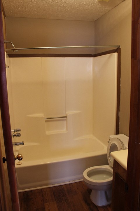 A white bathtub sits next to a toilet in a small bathroom.