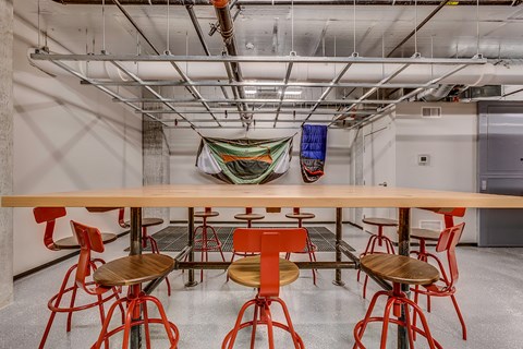A long wooden table surrounded by red chairs in a room with a concrete floor and ceiling.