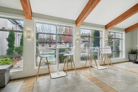 A room with a table and chairs in front of a window with a view of a pool and trees.