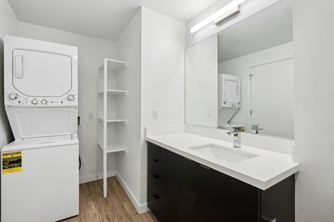 a white washer and dryer in a bathroom with a sink and a mirror