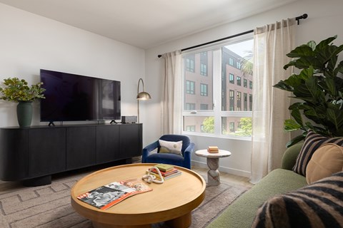 A living room with a flat screen TV on a cabinet and a sofa with a striped blanket on it.