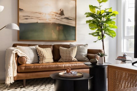 a living room with a brown couch and a painting on the wall