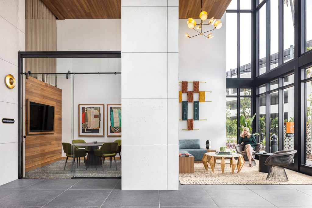 a living room and dining room with large windows and a woman sitting on a couch