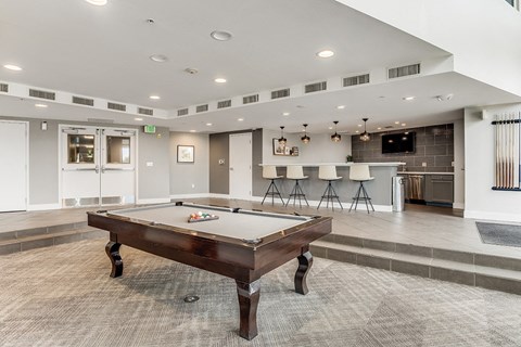 A pool table is in the middle of a room with a bar in the background.