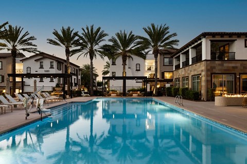 A swimming pool surrounded by palm trees and lounge chairs in front of a building.