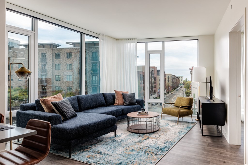 a living room with a blue couch and a rug and large windows