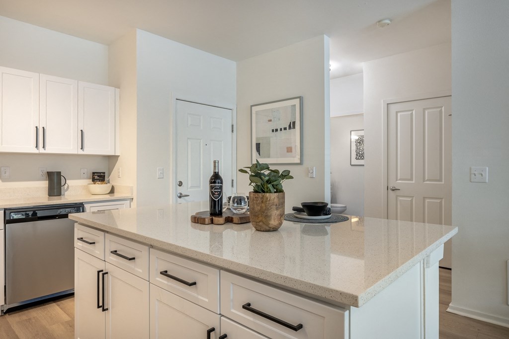 a kitchen with white cabinets and a large white island with a bottle of wine on it