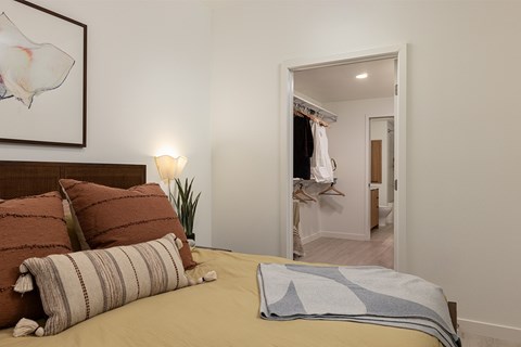 A bedroom with a bed, pillows, a lamp, and a painting on the wall.