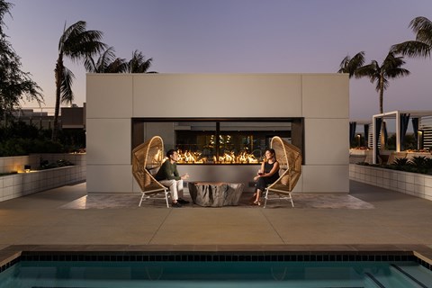 Two people sitting by a pool in front of a modern house.