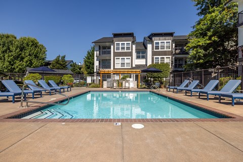 a swimming pool with chaise lounge chairs and umbrellas in front of an apartment building