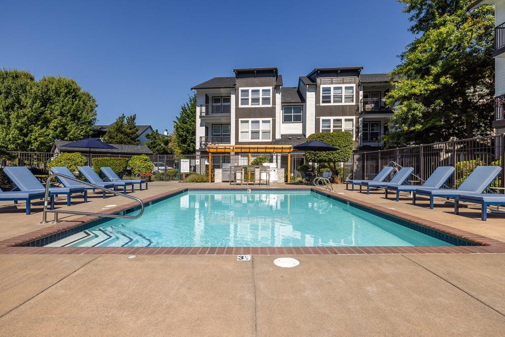 a swimming pool with chaise lounge chairs and umbrellas in front of an apartment building