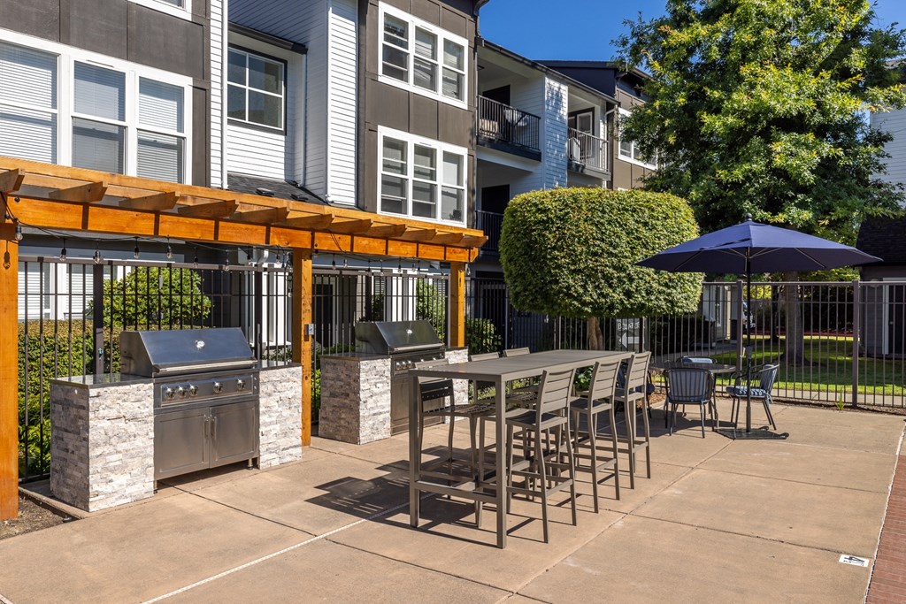 a patio with a grill and table with chairs and umbrellas