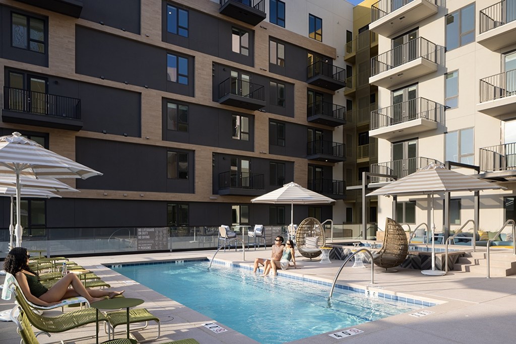 Two women are sitting by a pool in front of apartment buildings.
