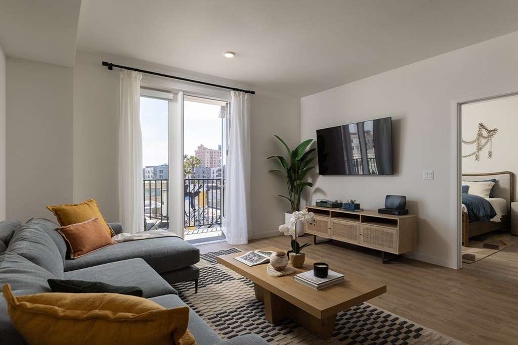 A living room with a grey couch, a wooden coffee table, and a large window with a view of the city.