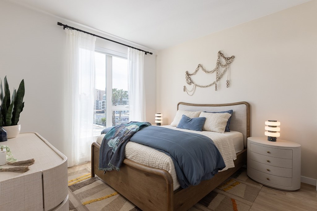 A bedroom with a bed, nightstand, and a plant.