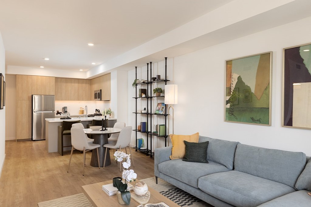 A modern living room with a grey sofa and a kitchen area in the background.