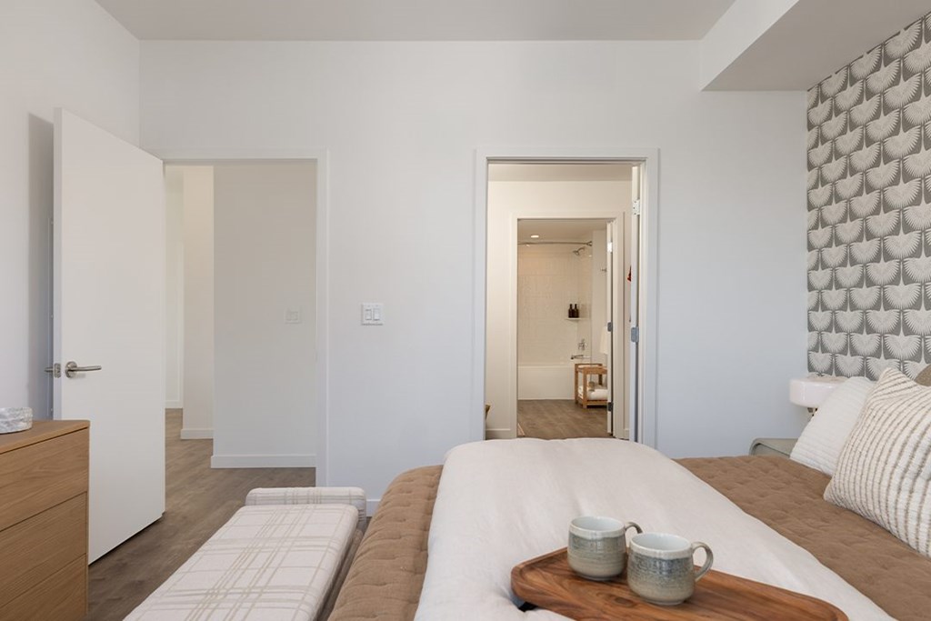 A bedroom with a large bed and a wooden tray with two cups on it.