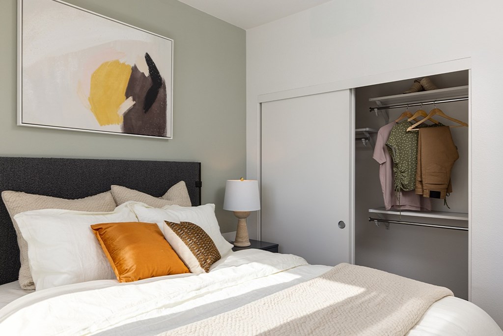 A bedroom with a bed, pillows, a lamp, and a painting on the wall.