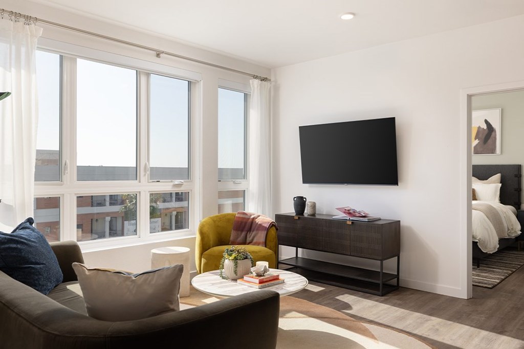 A living room with a large window, a yellow chair, a brown couch, and a flat-screen TV mounted on the wall.