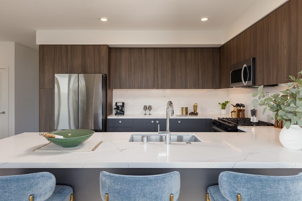 A modern kitchen with a white countertop and blue chairs.