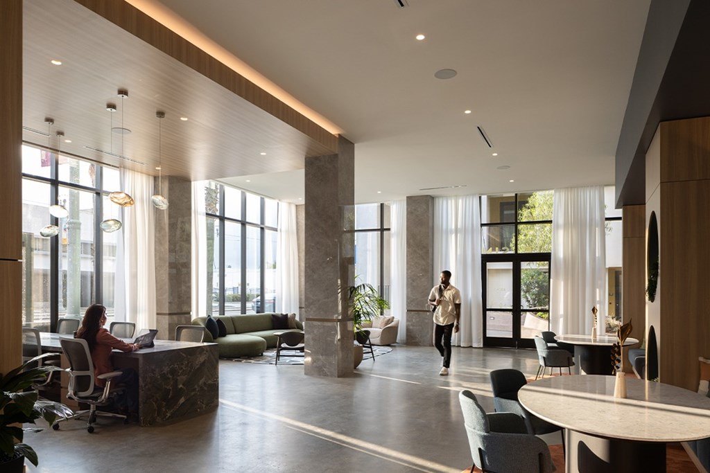 A woman is working on her laptop in a spacious office with large windows and natural light.