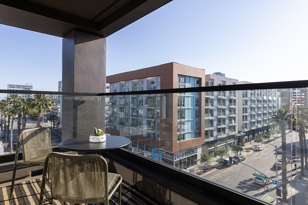A balcony with a table and two chairs overlooks a busy street.