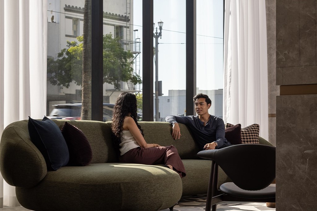 A man and woman are sitting on a couch in a room with large windows.