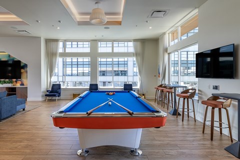 A pool table is in the middle of a room with a bar and a television.