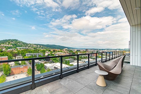 A modern chair and ottoman are placed on a balcony overlooking a cityscape.