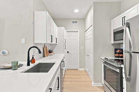 A kitchen with white cabinets and a black faucet.