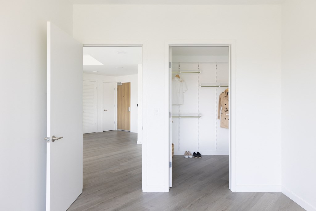 a hallway with white walls and a closet with shoes on the floor